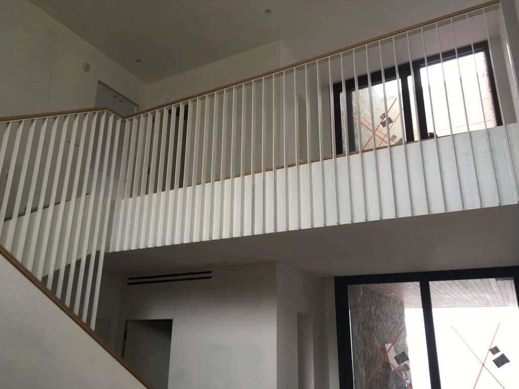 Interior de una casa en construcción con barandales blancos y ventanas grandes