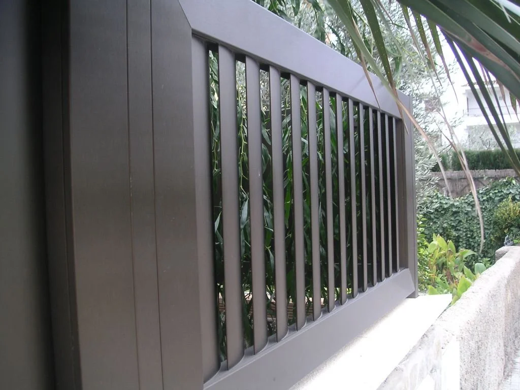 Reja de metal en una ventana en un entorno verde con plantas y arbustos.