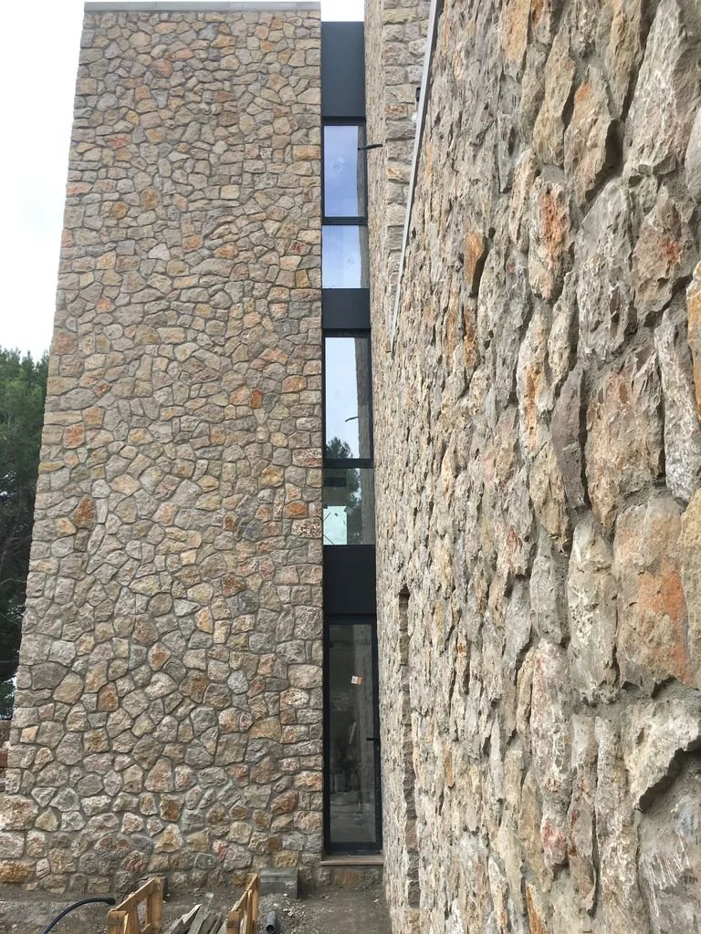 Vista frontal de un edificio con paredes de piedra y ventanas de vidrio enmarcadas en negro.