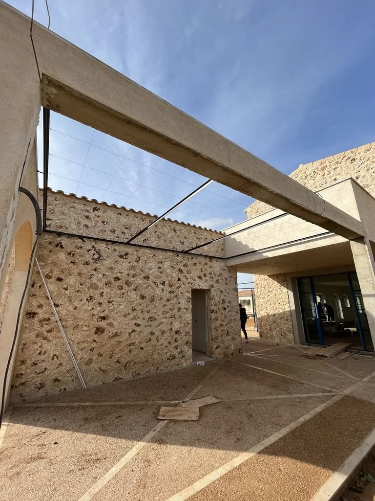 Construcción en proceso con estructura de acero y paredes de piedra y concreto en un espacio exterior.