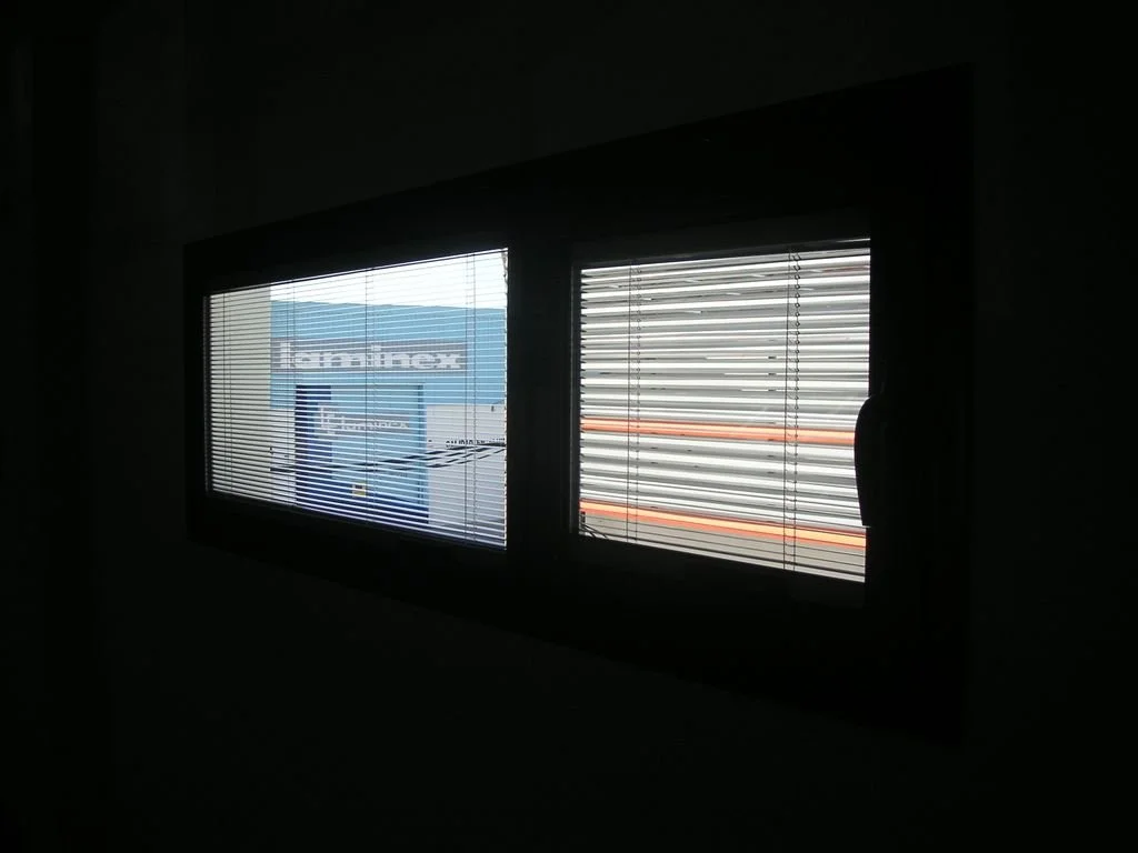 Ventanas con persianas en una habitación oscura, con vista a un edificio con letrero.