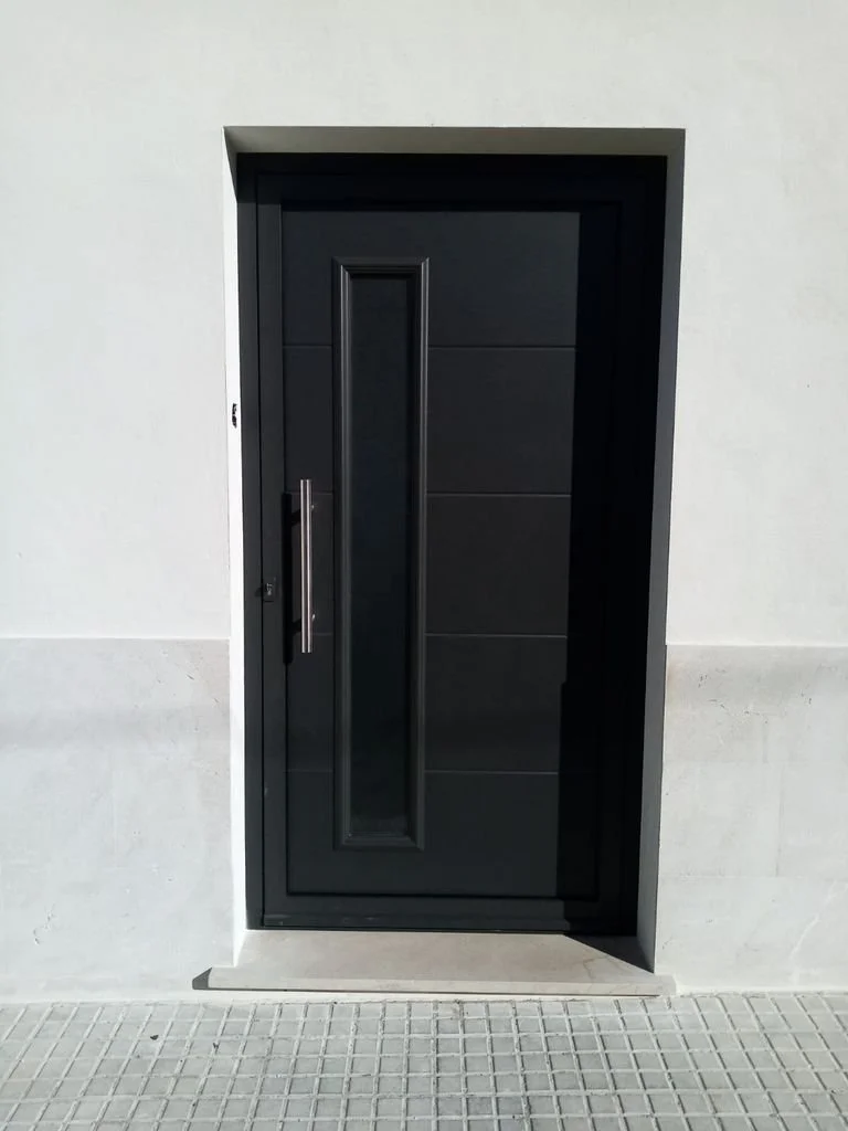 Puerta moderna de color negro con una manija larga en un edificio de ladrillo blanco.