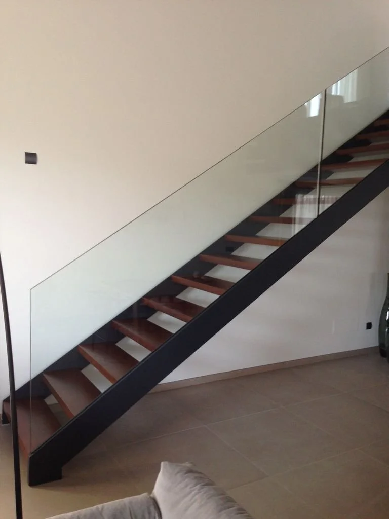 Escalera moderna de metal y madera con barandal de cristal en interior de casa.