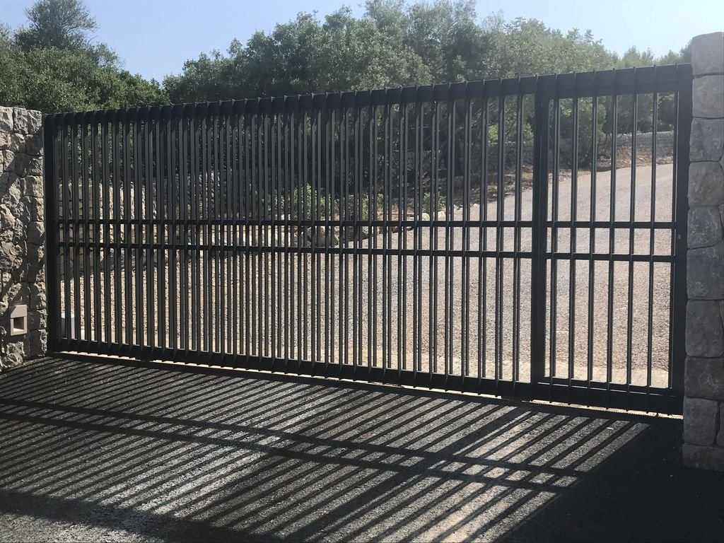Puerta automática de reja de metal con sombra en el suelo y paredes de piedra a los lados