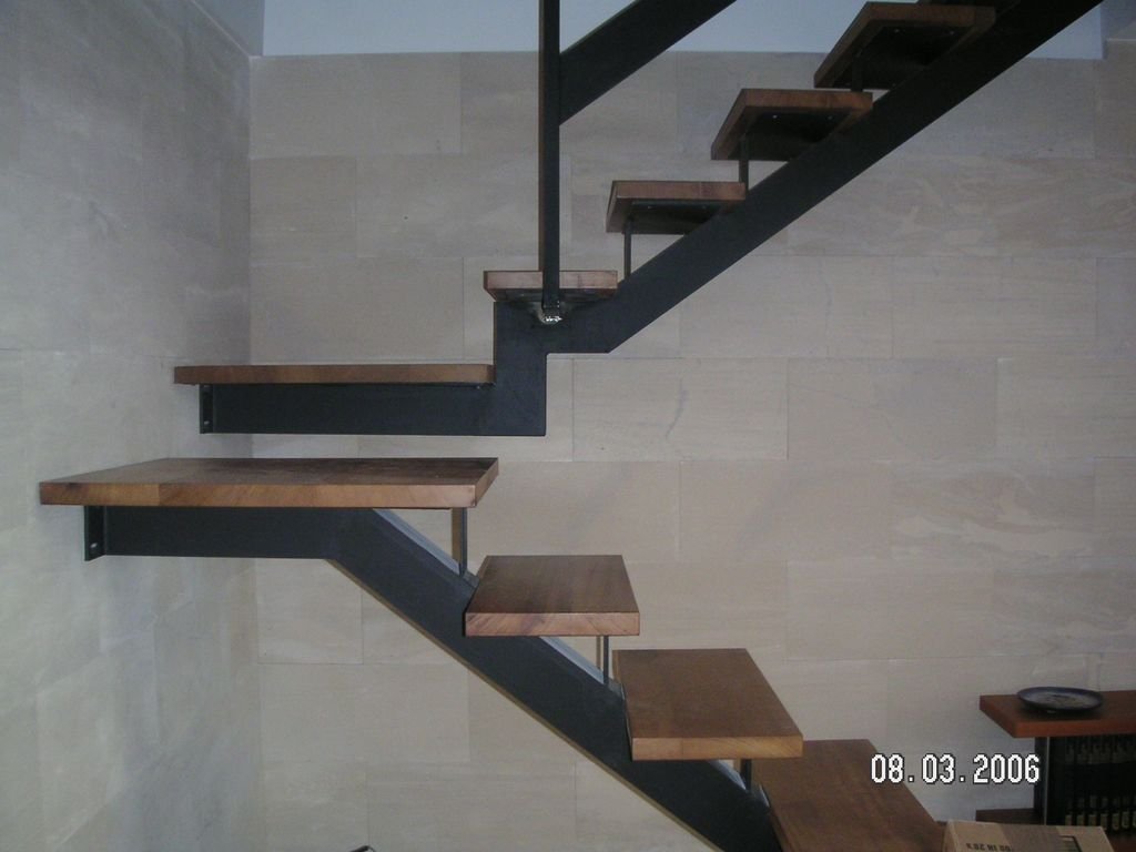 Escalera moderna de metal y madera en interior con paredes de yeso claro y piso de baldosas beige