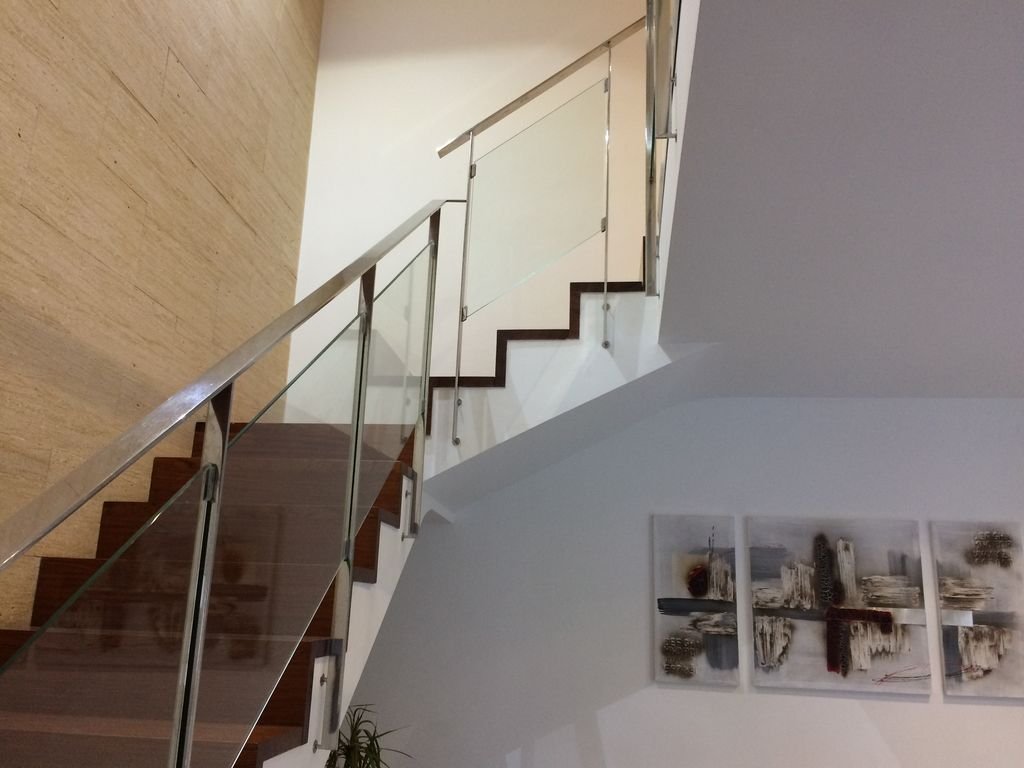 Escalera interior con barandal de metal y madera, paredes blancas, y obra de arte decorativa en la pared.