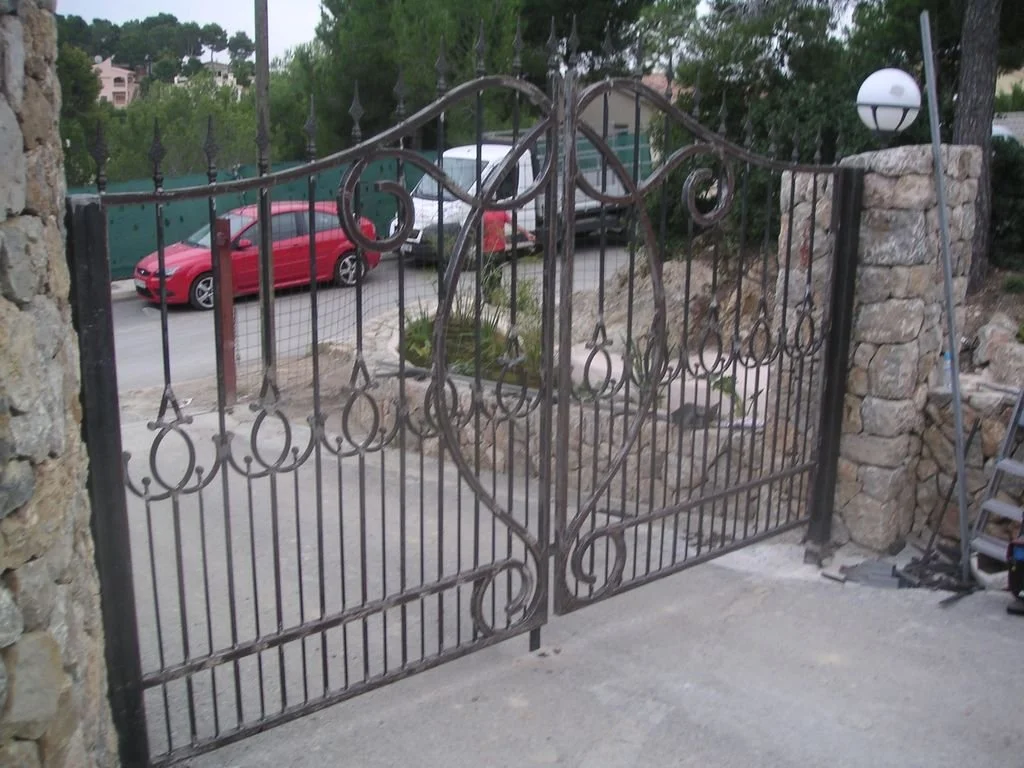 Puerta de reja de metal con diseño ornamental en un muro de piedra.