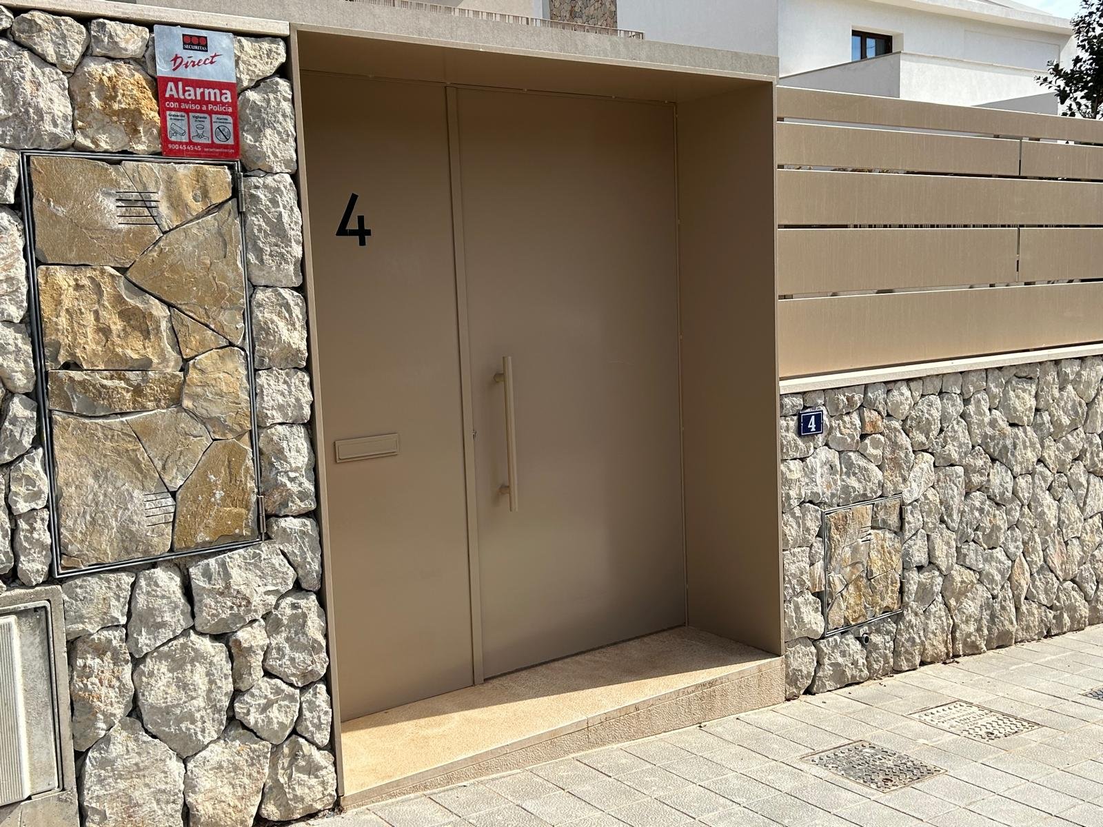 Puerta de entrada de un edificio con muro de piedras y números 4 en la puerta y en una placa en la pared.