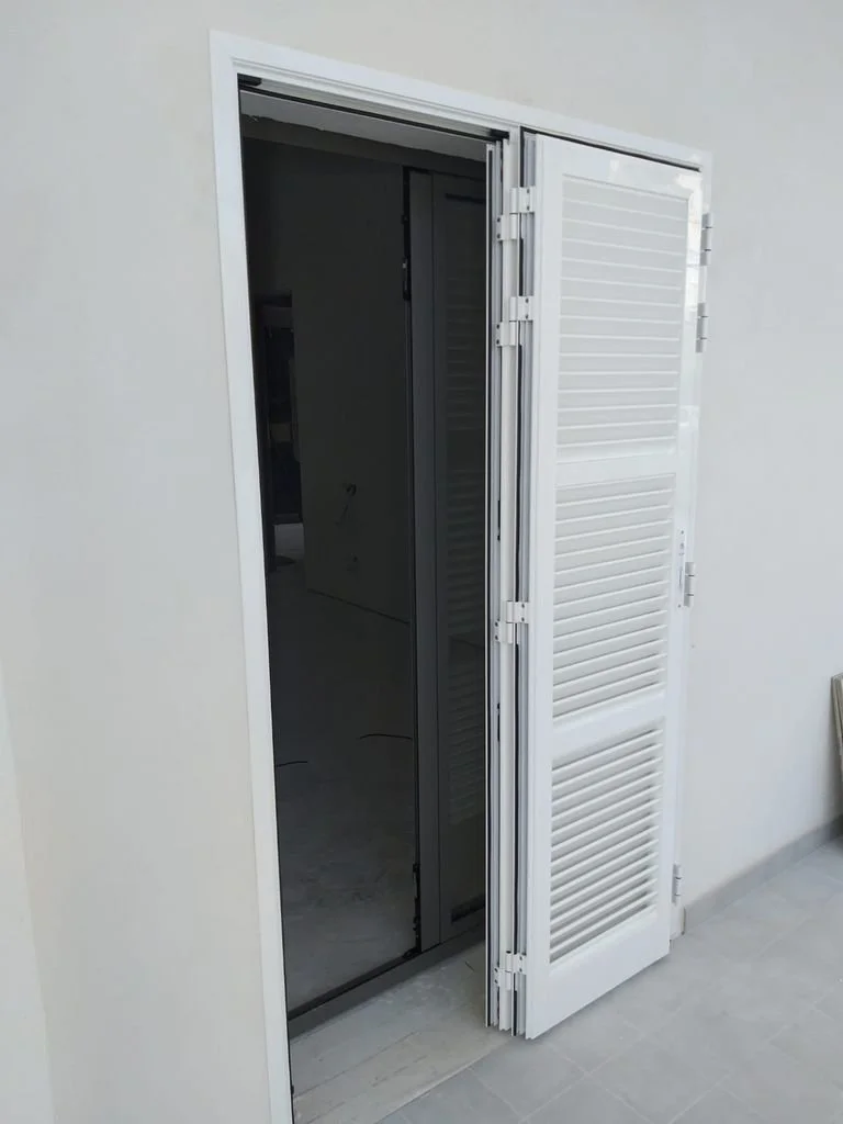 Puerta corrediza de vidrio y persianas blancas en una pared blanca, con piso de baldosas grises.