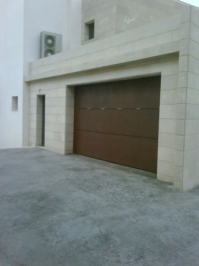Vista frontal de una cochera con puerta de madera y muro de piedra.