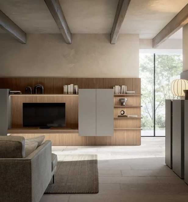 Interno di un soggiorno con parete attrezzata in legno, televisore, librerie con libri e decorazioni, grande finestra con vista su alberi verdi.