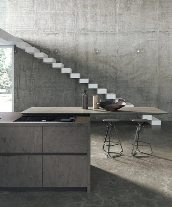 Interno moderno con cucina in stile minimalista, tavolo in legno con due sgabelli, scale in stile sospeso e pareti di cemento grezzo.