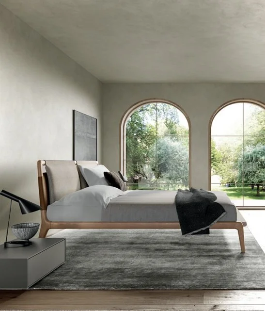 Una camera da letto minimalista con letto a baldacchino, grandi finestre ad arco con vista su un giardino verde, e arredi semplici e moderni.
