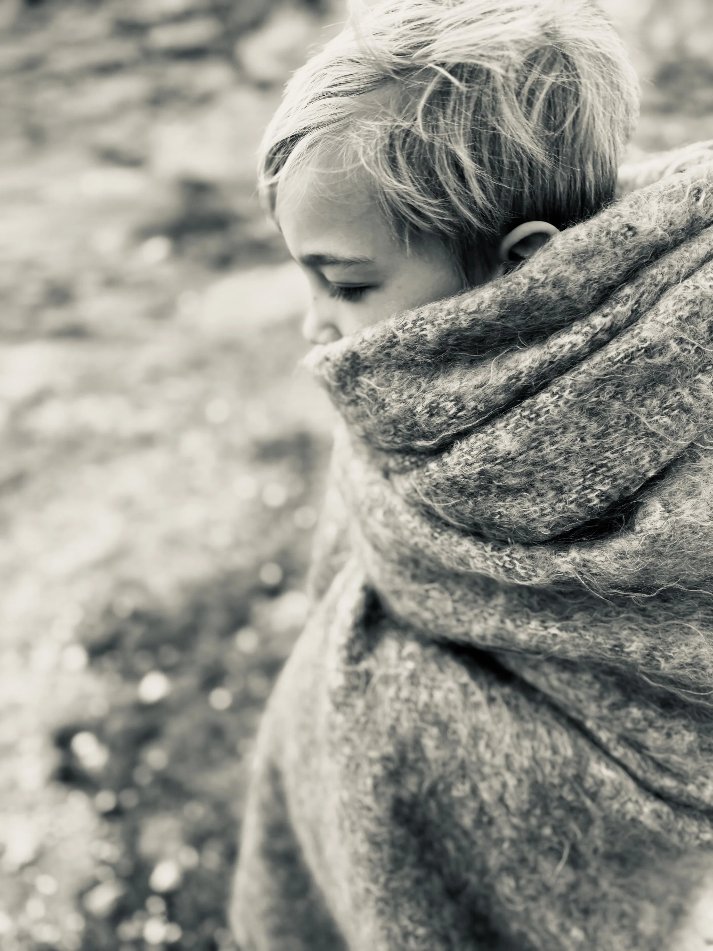 A young boy with wrapped in a large mohair scarf outdoors.
