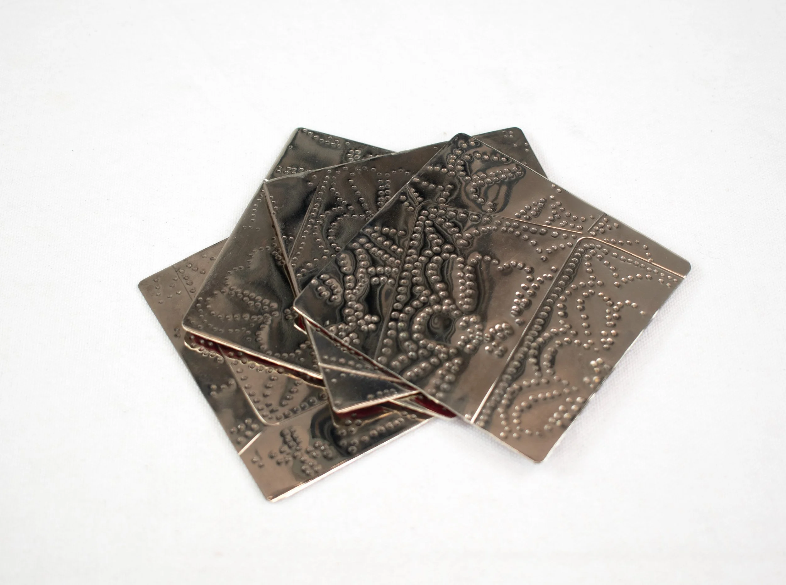 A pile of metal cards with intricate, raised dotted patterns on a white background.