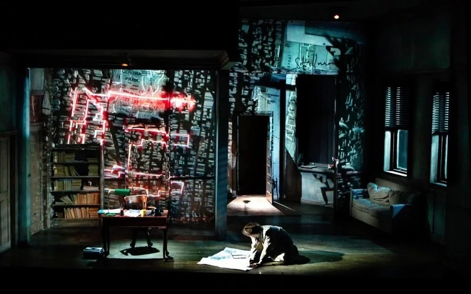Dimly lit room with a person on the floor using a flashlight to read papers, a bookshelf, and a window with pelmeted curtains; walls cast shadow patterns due to daylight filtering through blinds.