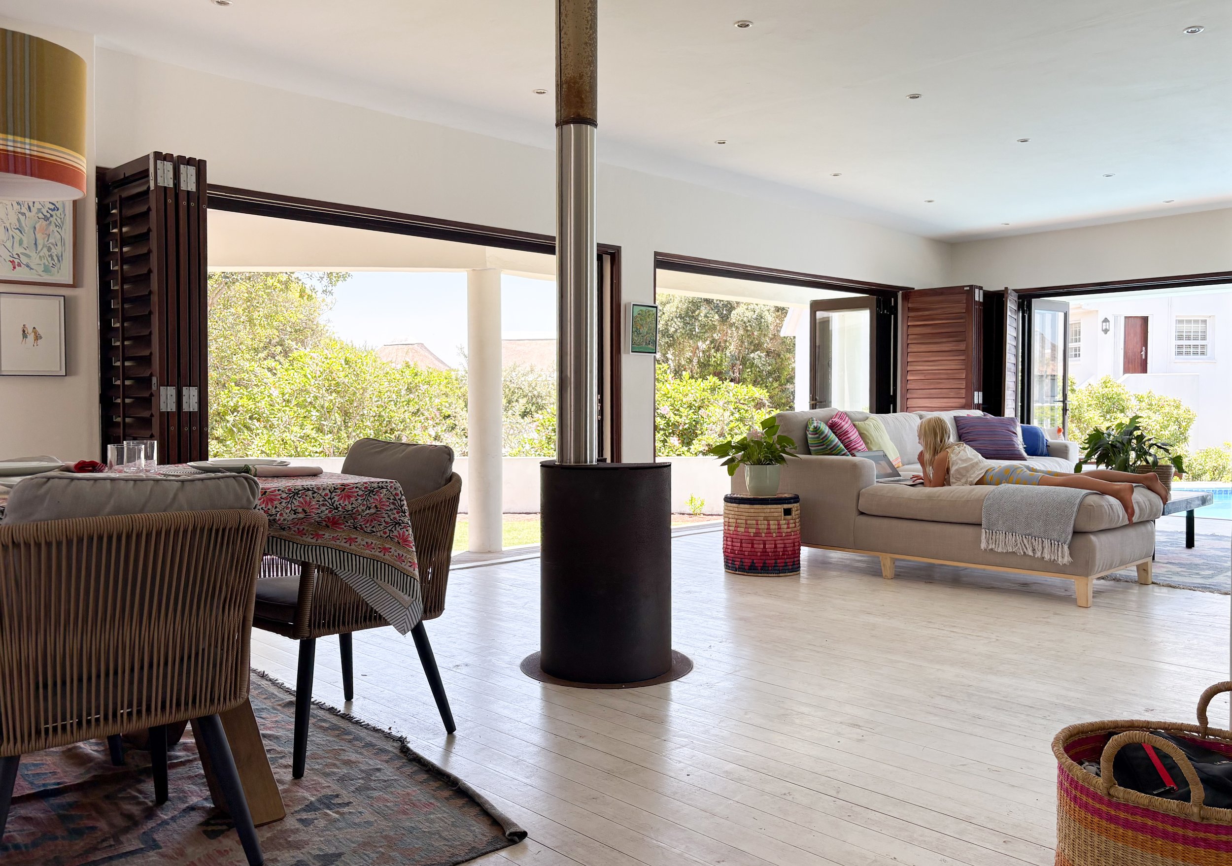 Open-plan lounge and dining area with log burner, pool and garden visible beyond