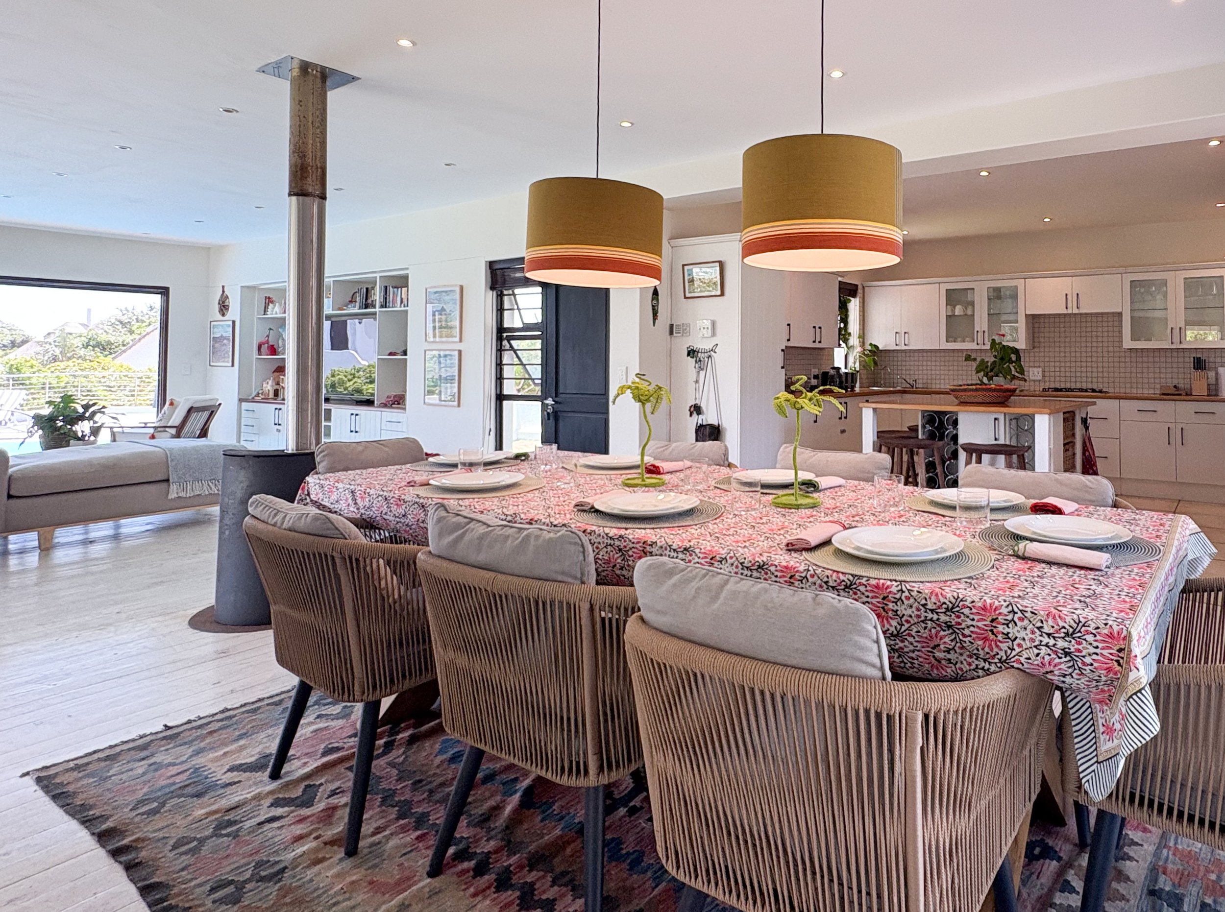 Dining table set for a large group beneath pendant lights, log burner and kitchen beyond