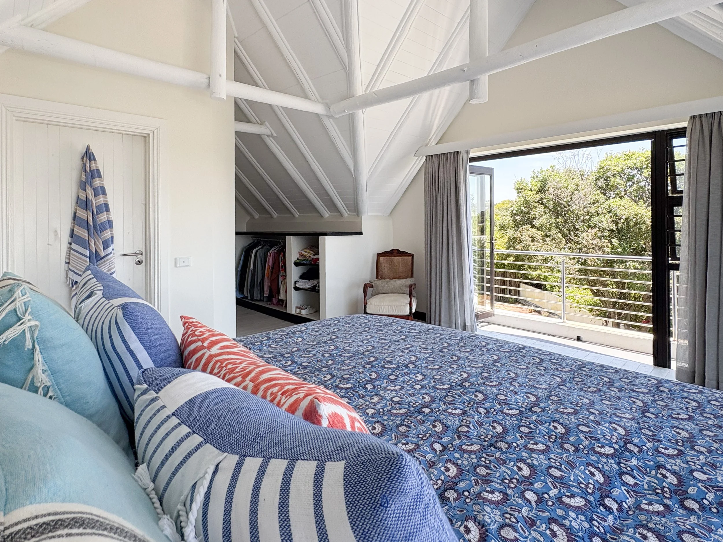 Blue and white bedding with balcony and treetop view beyond