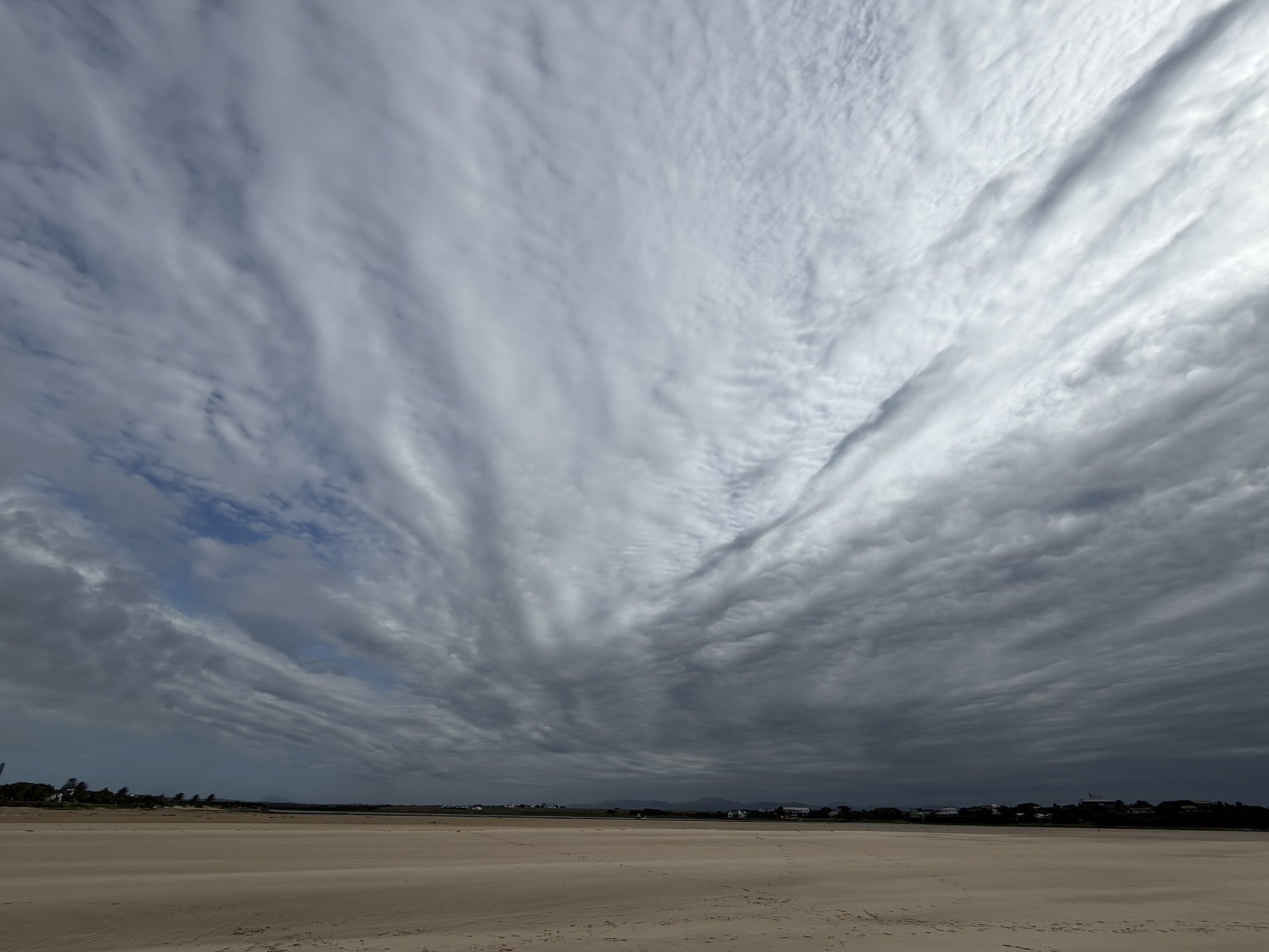 A wide, open landscape with a flat, sandy surface under a dramatic, cloudy sky.