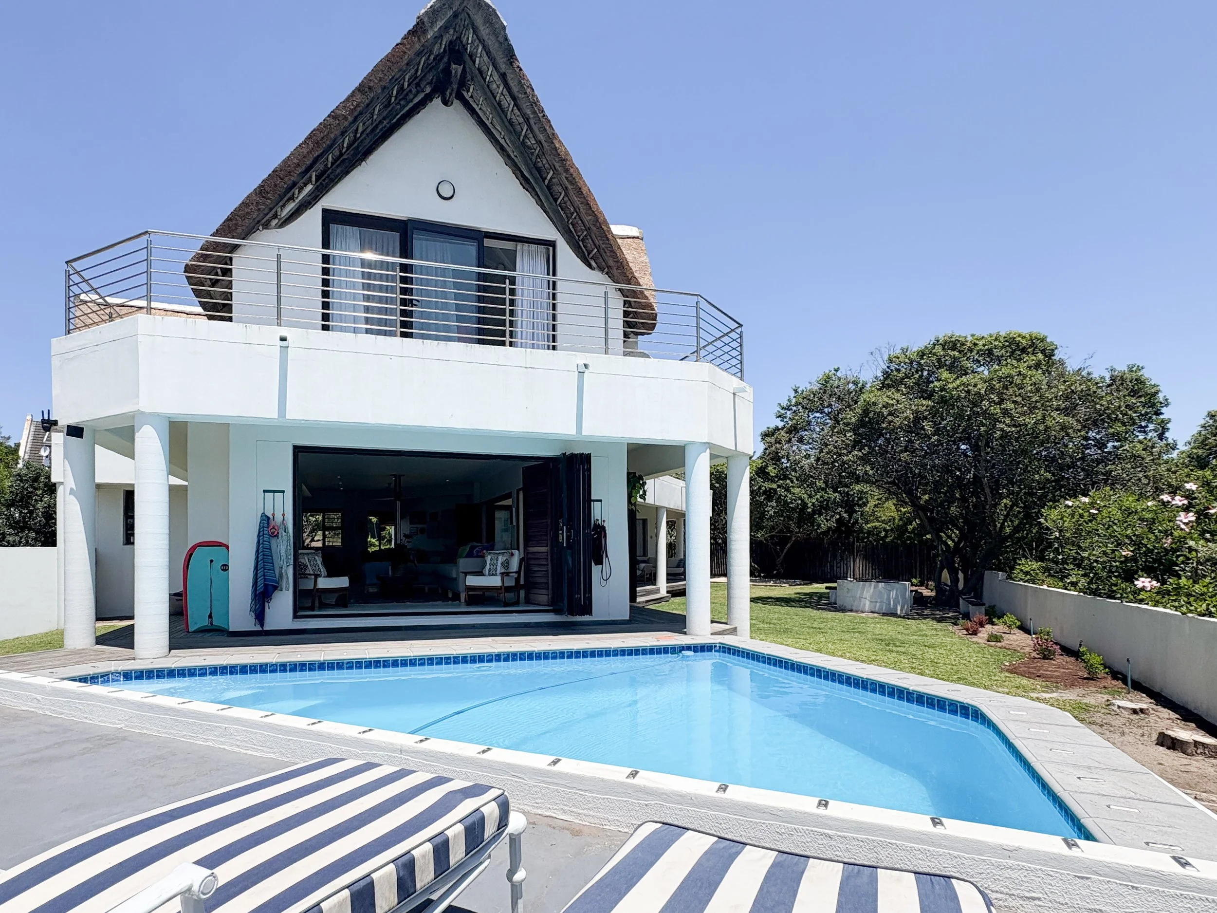 Ground-level view of the house and pool from the garden, thatched gable and balcony visible