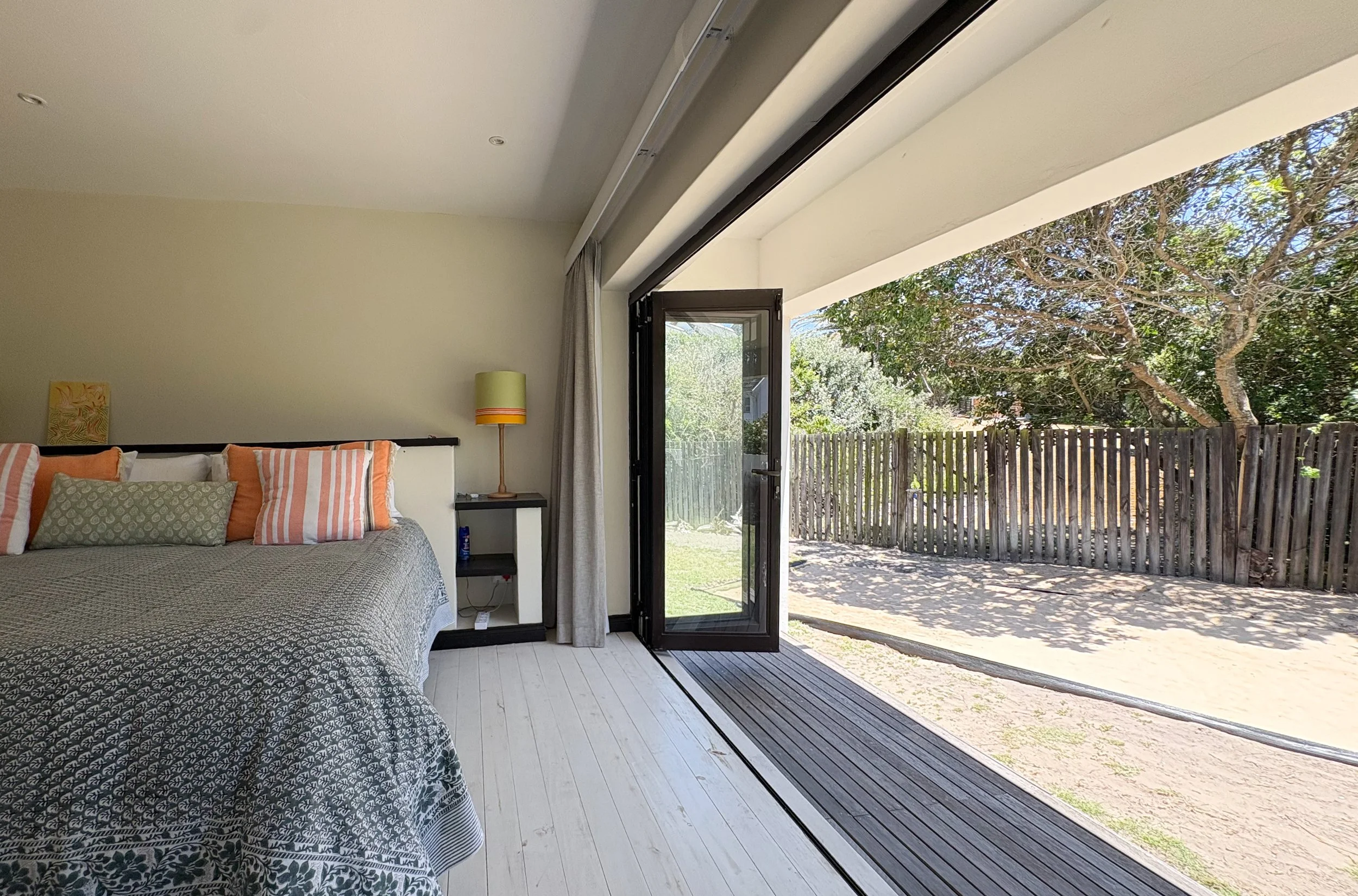 Bed beside folding doors opening onto a sheltered deck