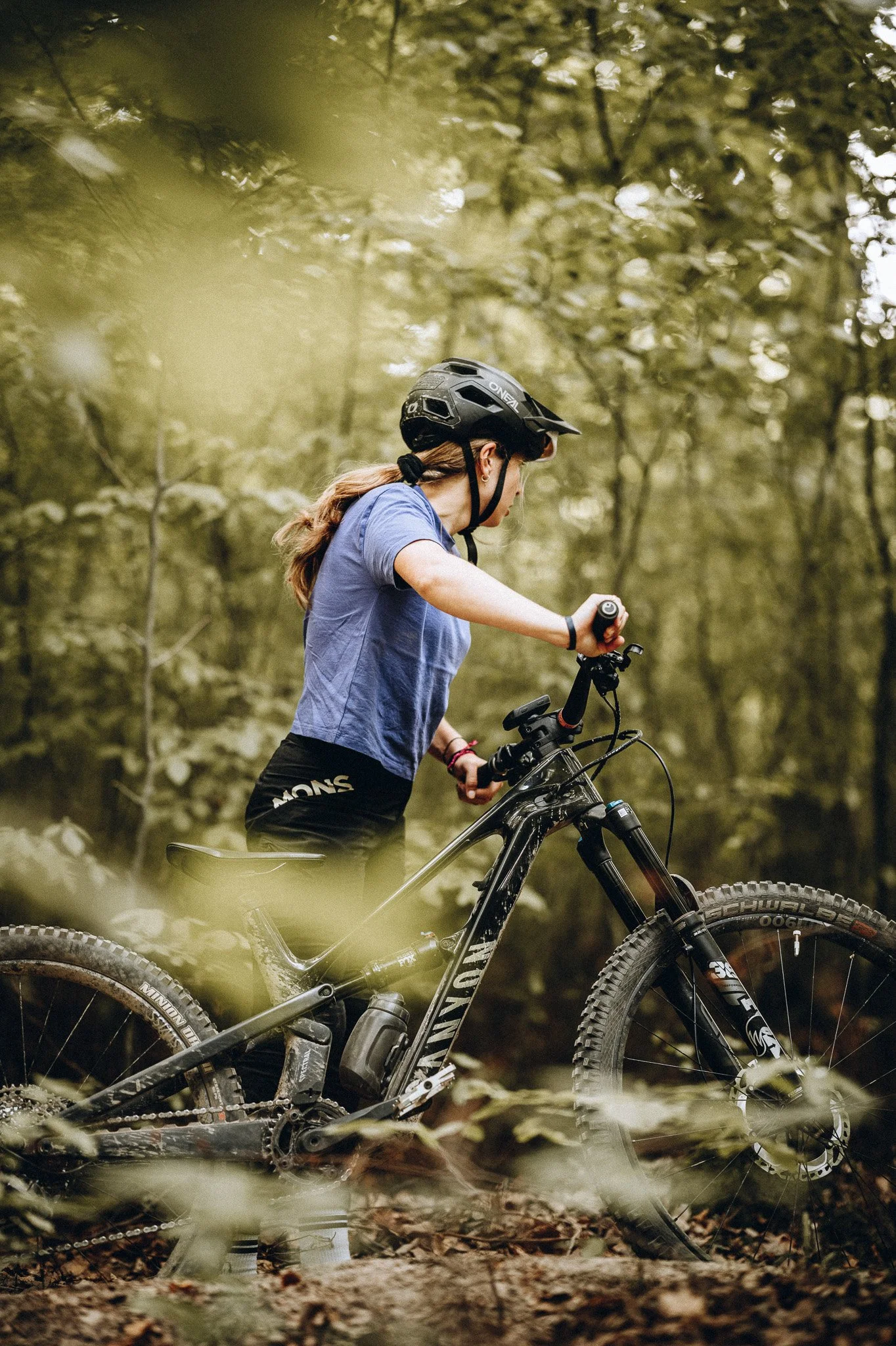 Frau mit Fahrrad in einem Wald, trägt Schutzhelm, blaue T-Shirt, schwarze Shorts, fährt Mountainbike auf einem schmalen Weg. Marvin Lahrs Sport Mountainbike Fotograf