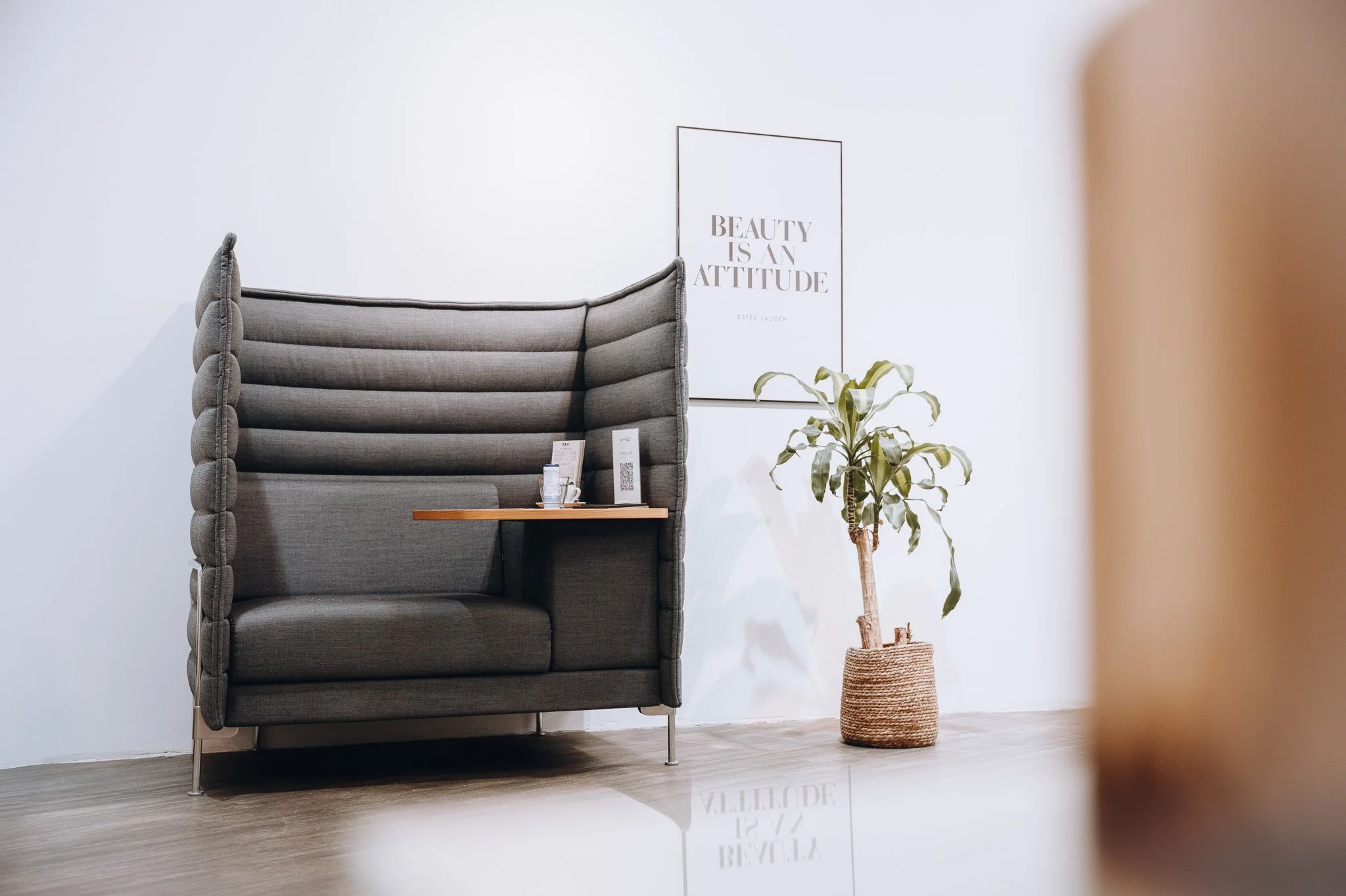 Ein graues, modernes, zeltartige Sofa in einem Raum neben einer Topfpflanze und einem Rahmen mit dem Spruch "Beauty is an Attitude" auf der weißen Wand. Marvin Lahrs Businessfotograf aus Koblenz