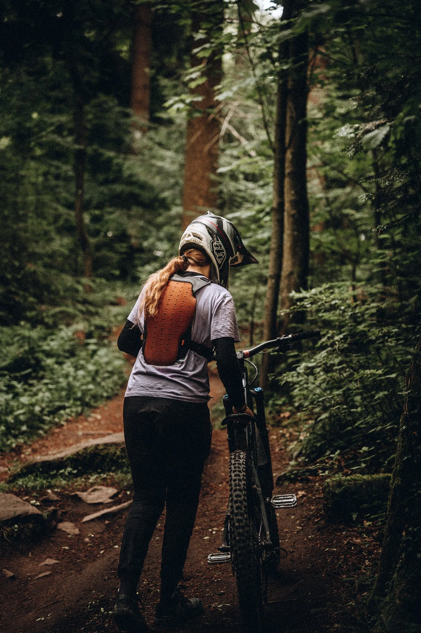 Frau mit Fahrrad in einem dichten, grünen Wald, trägt Helm und Fox Protektor. Marvin Lahrs Sport Mountainbike Fotograf