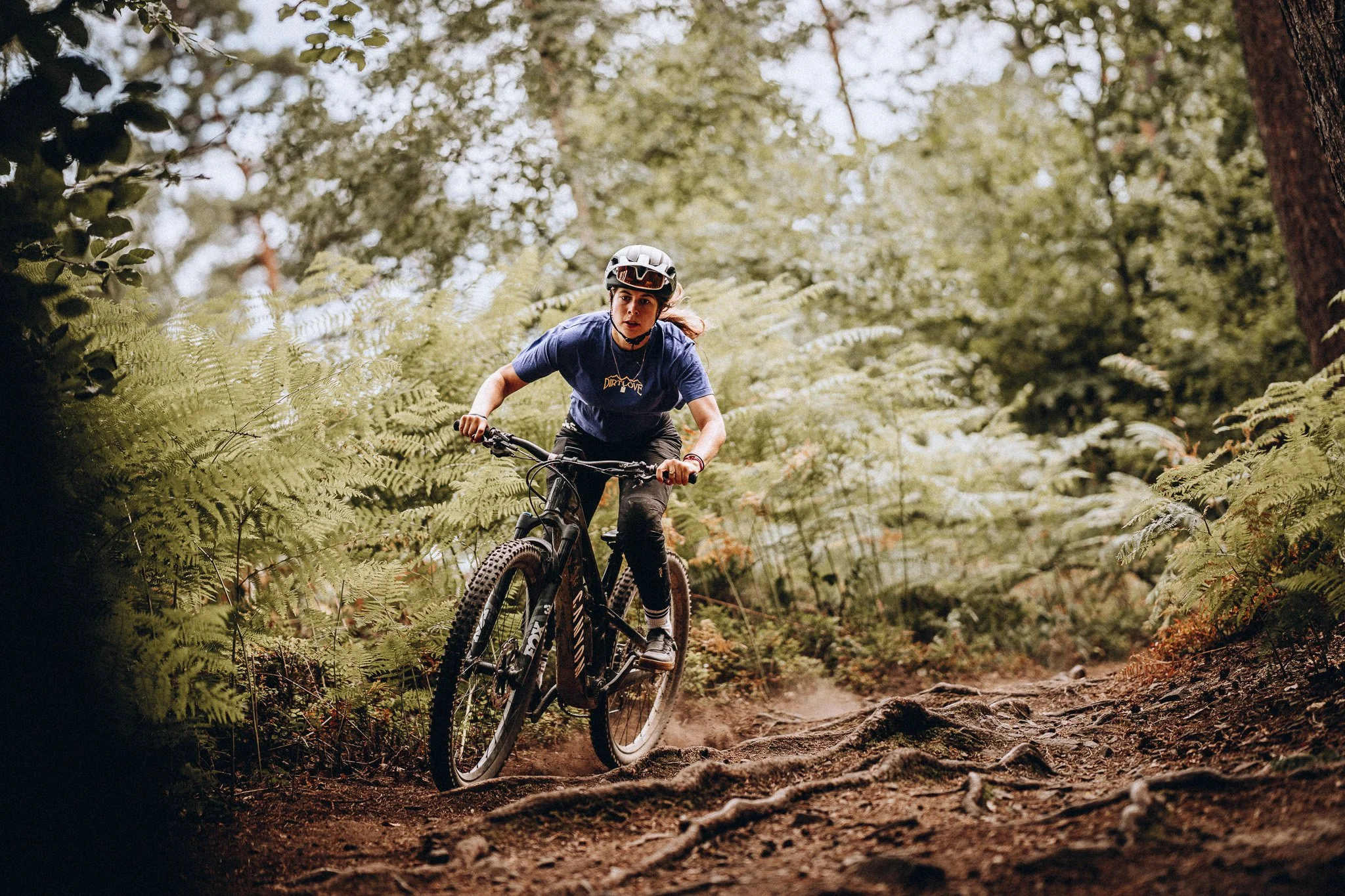 Frau fährt Mountainbike auf einem Waldweg, umgeben von grünen Bäumen und Blättern, trägt Fahrradhelm und sportliche Kleidung. Marvin Lahrs Sport Mountainbike Fotograf