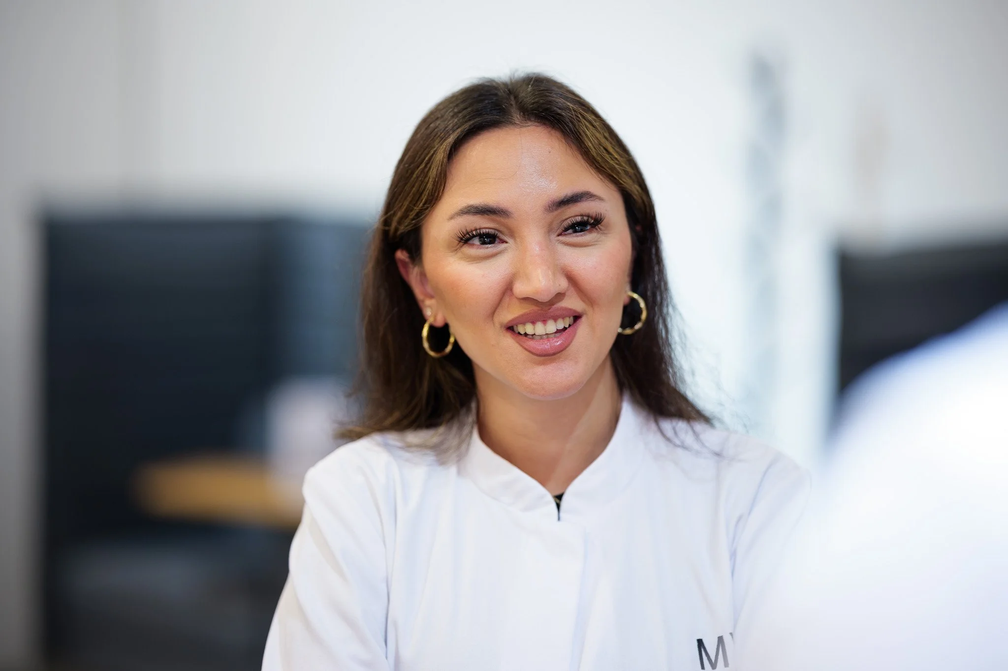 Eine lächelnde Frau mit braunen Haaren und goldenen Ohrringen, trägt eine weiße medizinische Jacke, in einem medizinischen Umfeld. Marvin Lahrs Businessfotograf aus Koblenz