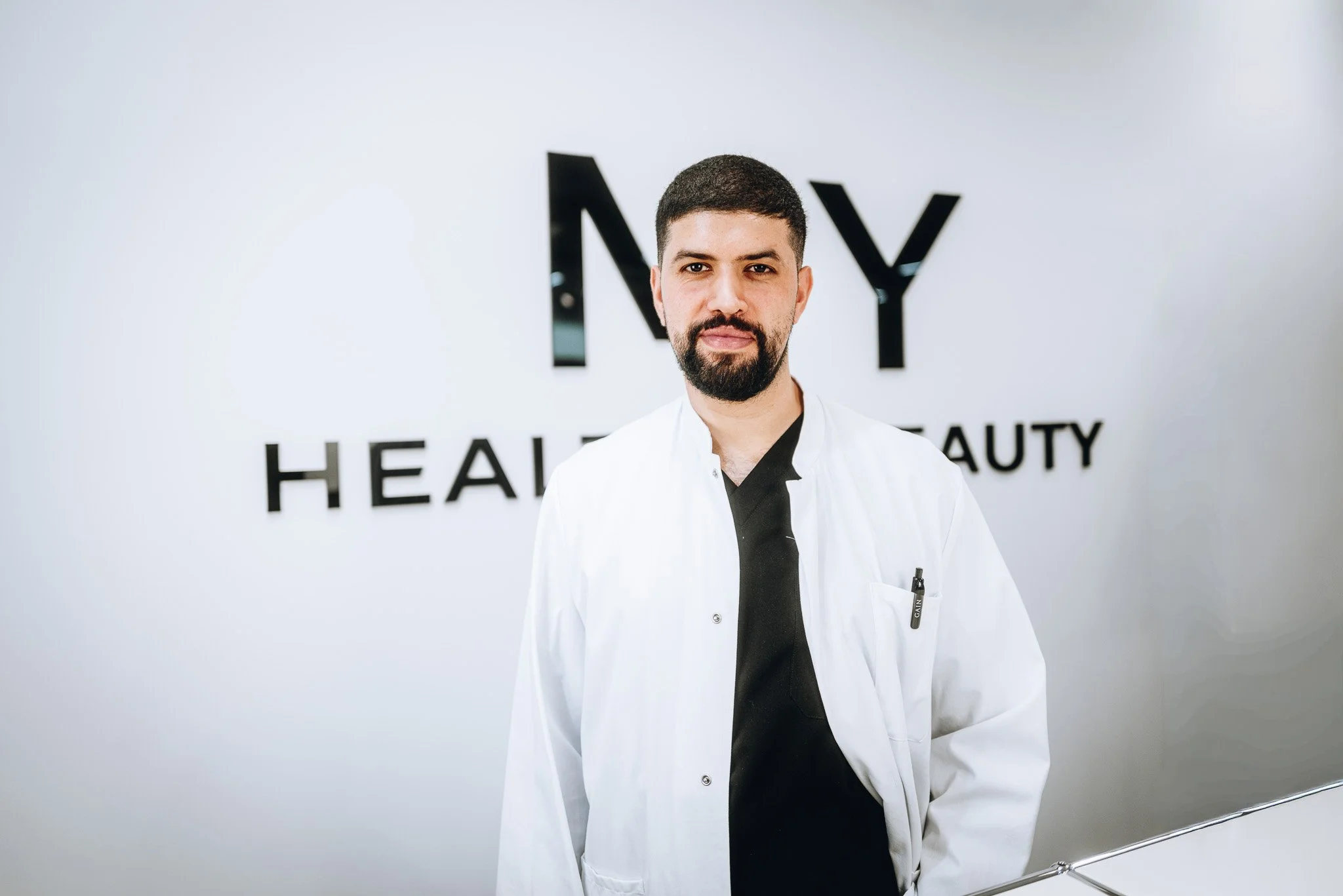 Mann in weißem Arztkittel vor einem weißen Hintergrund mit schwarzen Buchstaben, die 'MY' und 'HEALTH & BEAUTY' bedeuten. Marvin Lahrs Businessfotograf aus Koblenz