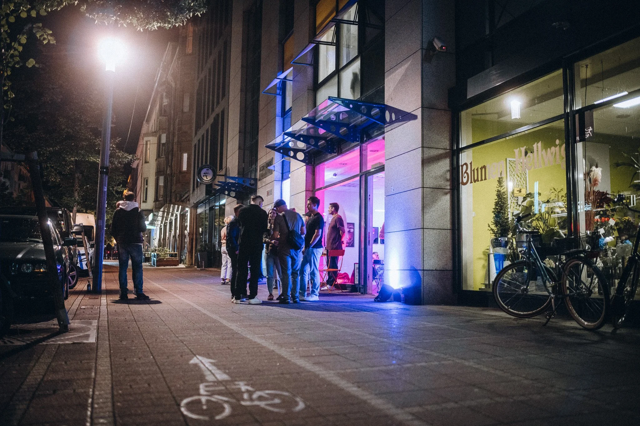 Abendliche Straße mit beleuchteter Galerie und Besuchern – Eventfotografie bei Nacht