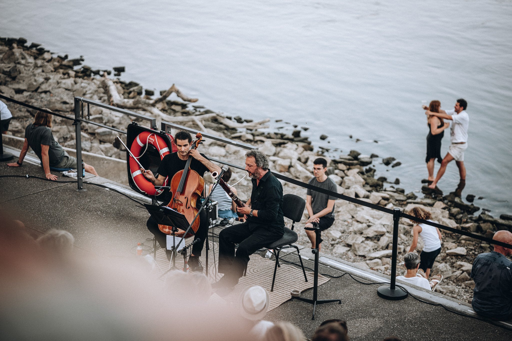 Musiker spielen am Strand auf einer Open-Air-Bühne, während Menschen am Ufer spazieren und sich unterhalten. Marvin Lahrs Event Sport Fotograf Koblenz
