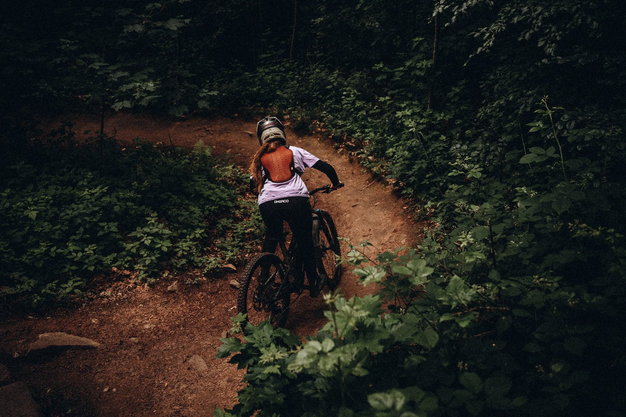 Eine Person fährt Mountainbike auf einem schmalen Weg durch einen dichten Wald bei Dämmerung. Marvin Lahrs Sport Mountainbike Fotograf