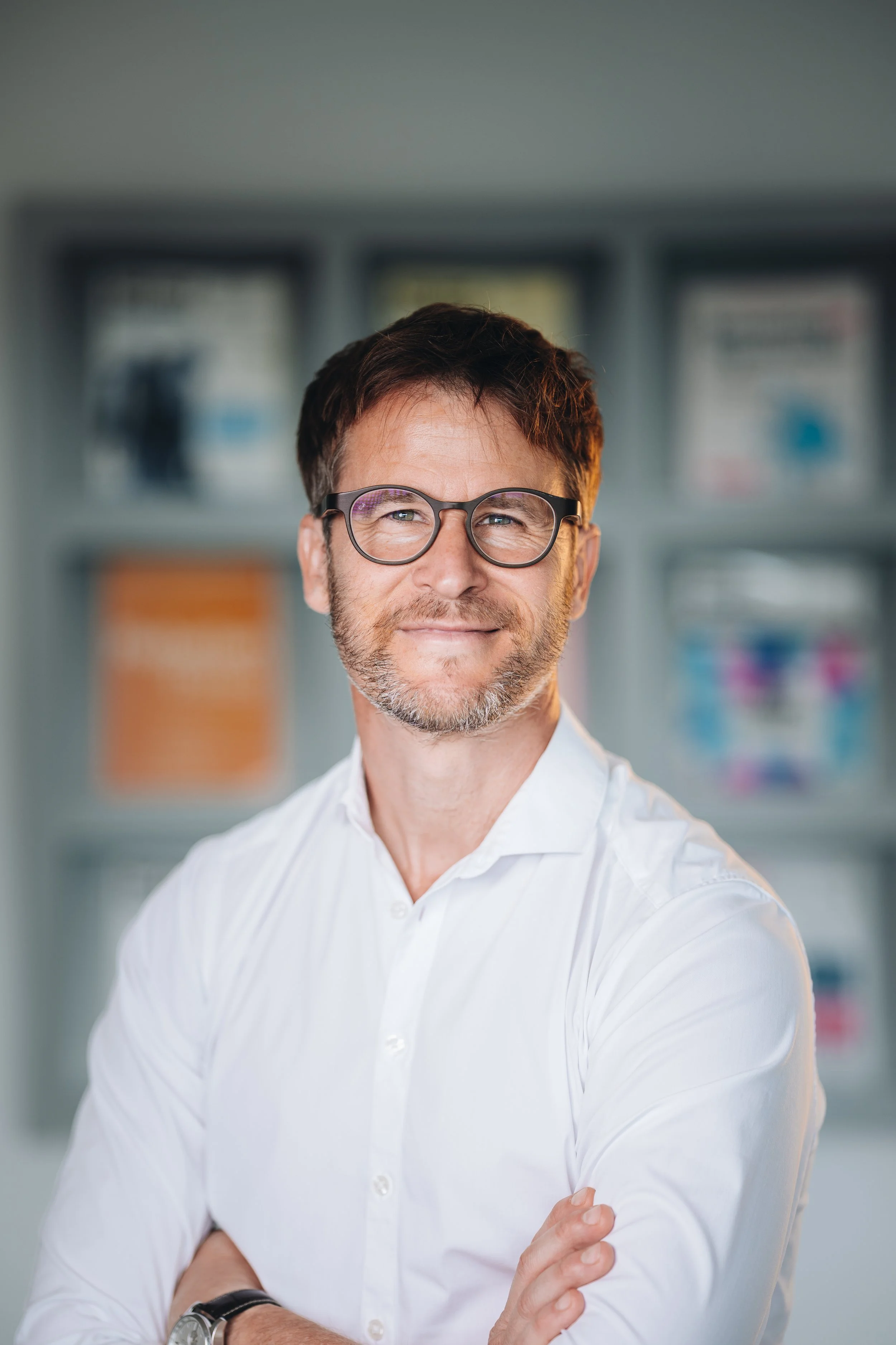 Business-Portrait eines lächelnden Mannes mit Brille und weißem Hemd vor Bücherregal – Businessfotograf Koblenz
