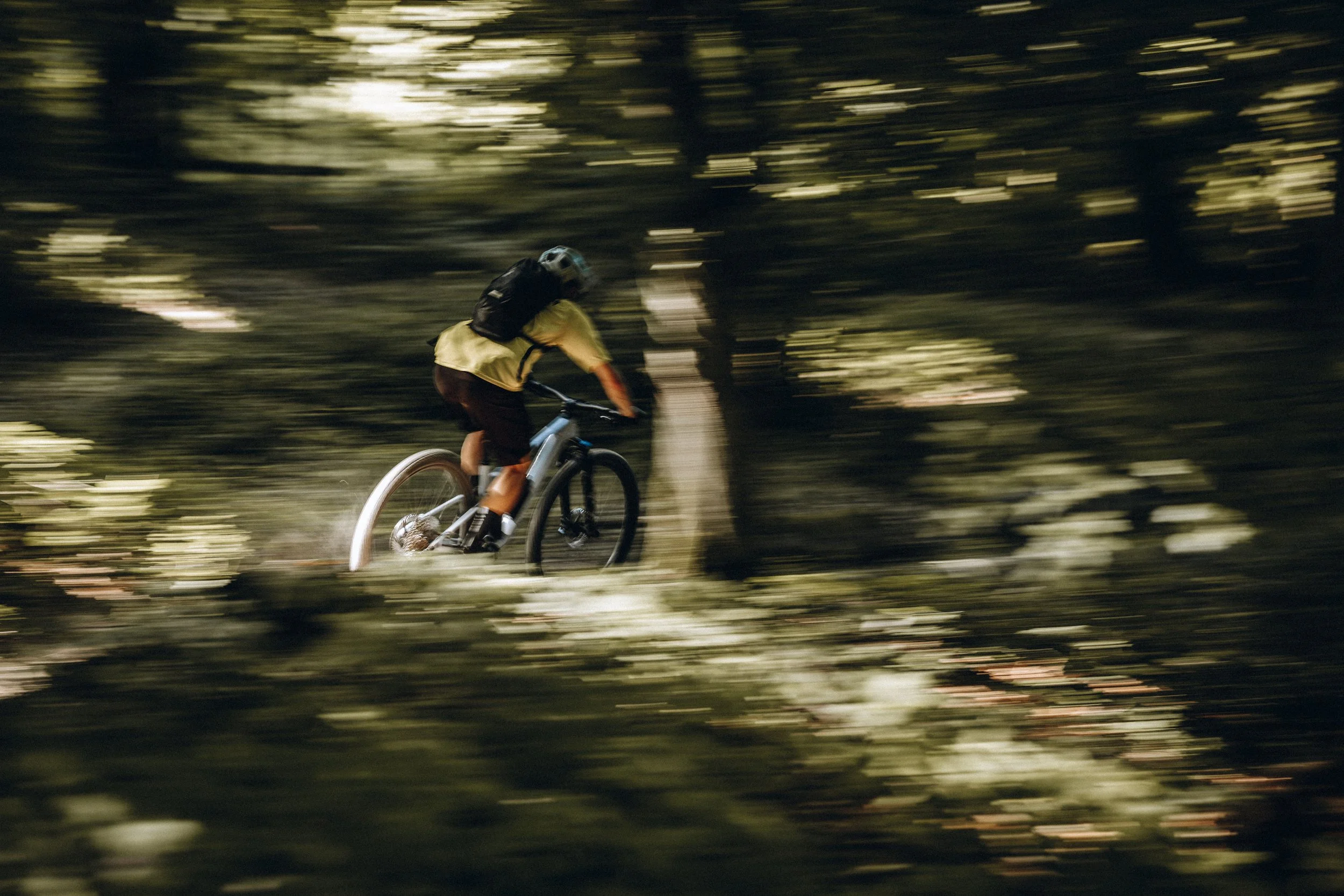 Radfahrer in rasanter Fahrt durch einen dichten Wald bei Dämmerung, mit verschwommenem Hintergrund. Marvin Lahrs Sport Mountainbike Fotograf