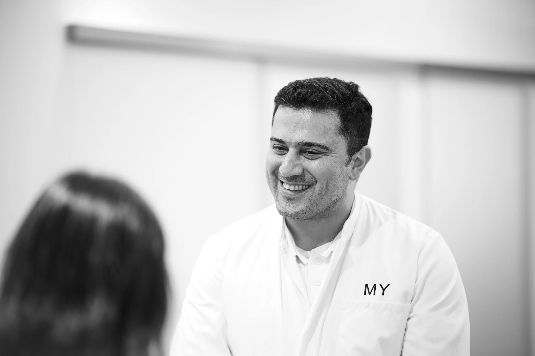 Lächelnder Mann in einer weißen Chefjacke, spricht mit einer Person vor ihm in einem weißen Raum. Marvin Lahrs Businessfotograf aus Koblenz