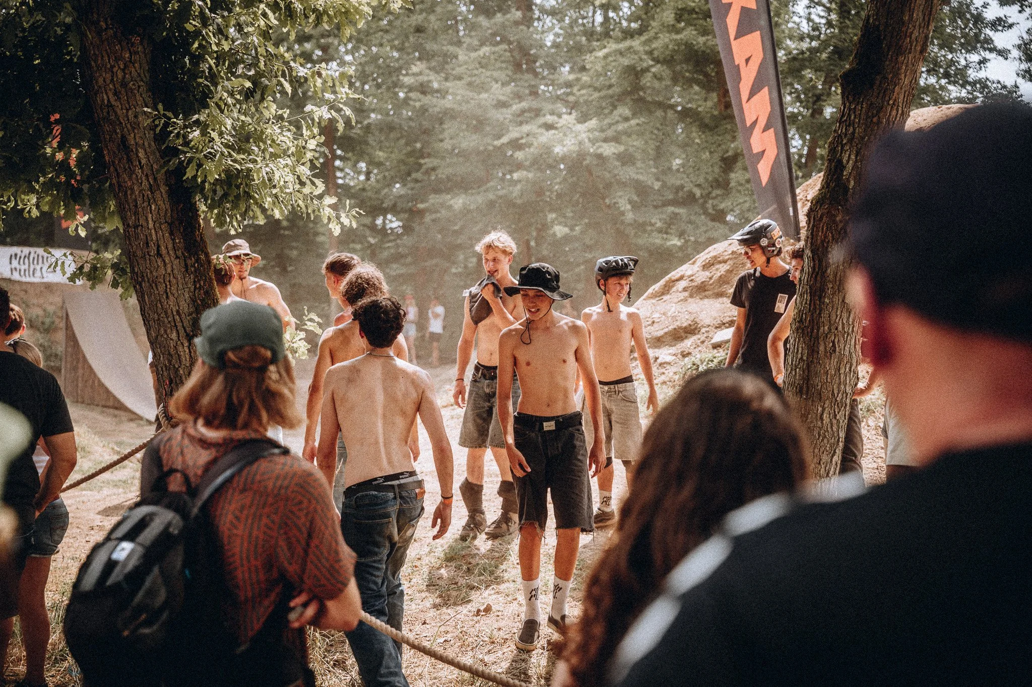 Gruppe junger Männer, einige ohne Oberkörper, mit Fahrradhelmen, die an einem Baum im Wald entlanglaufen, während andere Menschen im Hintergrund zuschauen.Marvin Lahrs Event Sport Fotograf