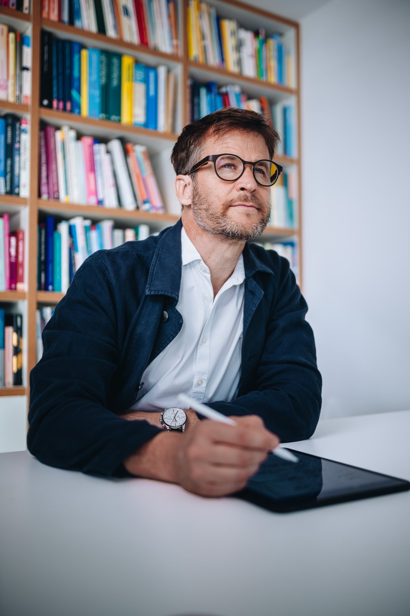 Mann im Sakko am Schreibtisch vor Bücherregal – Business-Portrait für Unternehmen