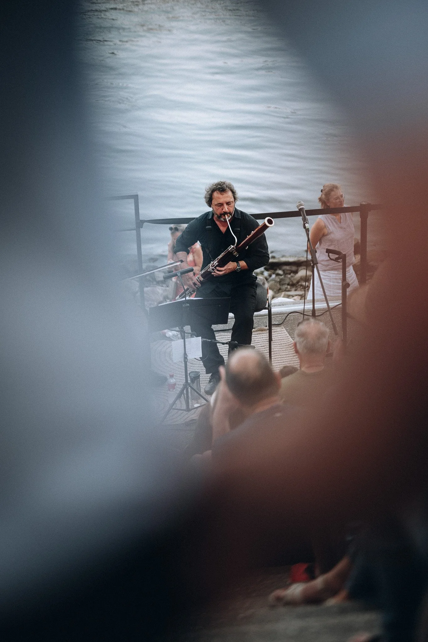 Musiker spielt ein langhornähnliches Instrument am Wasser, umgeben von Leuten, im Hintergrund bei Sonnenuntergang.Marvin Lahrs Event Sport Fotograf