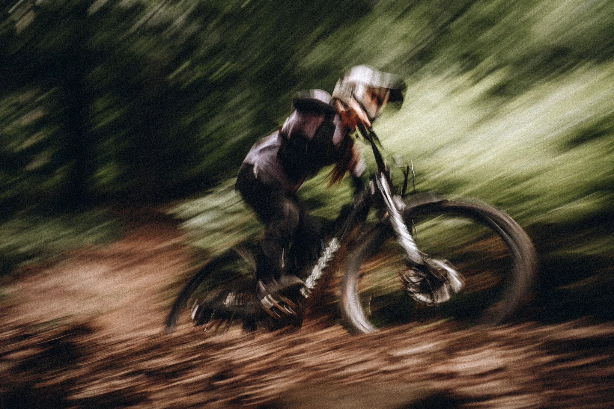 Ein Mountainbike-Fahrer fährt durch einen Wald mit hoher Geschwindigkeit, die Bewegungsunschärfe zeigt die Dynamik des Rennens.
zeigt Sport Fotografie