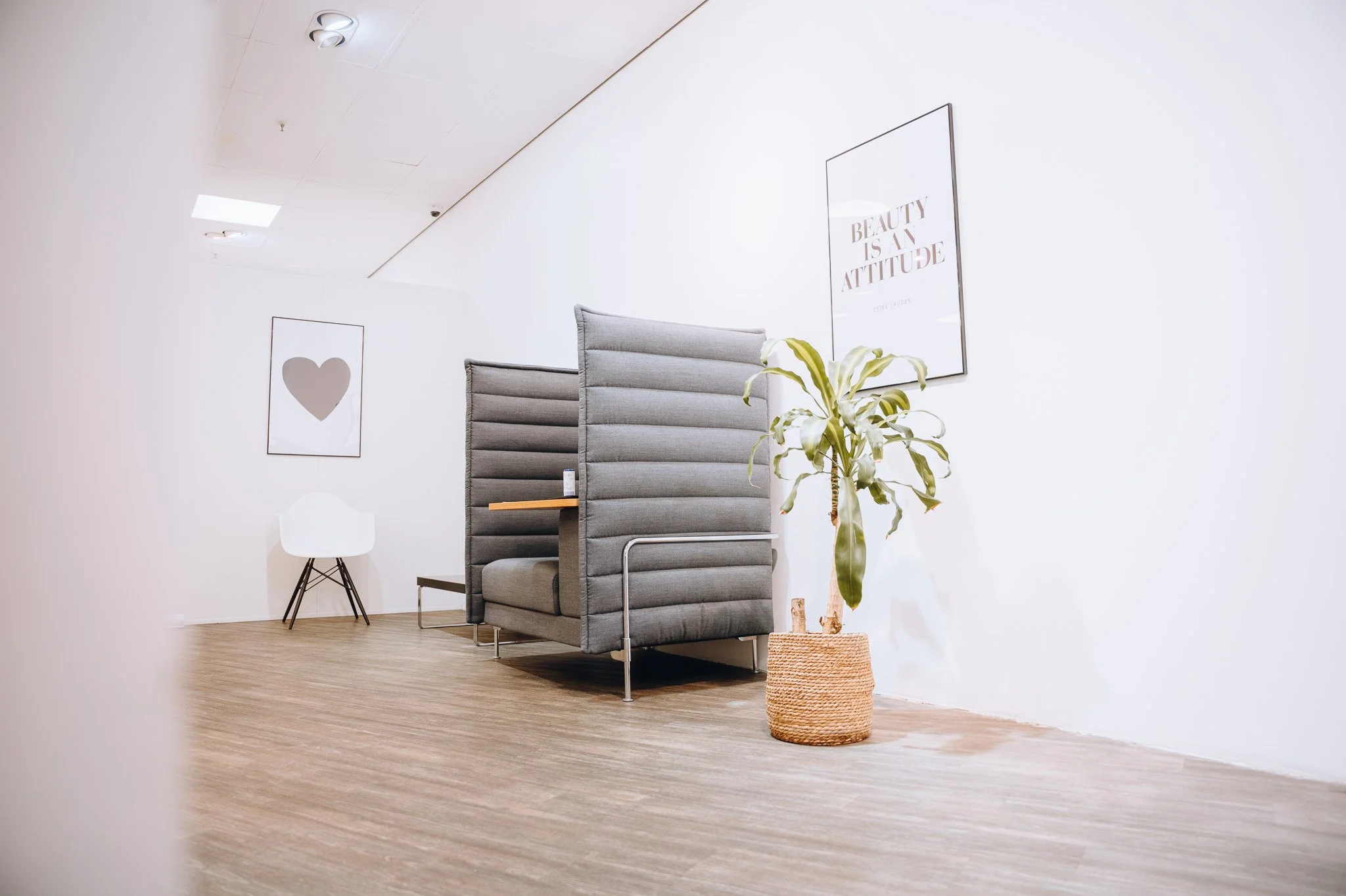 Ein modernes Wartezimmer mit einem hohen, gepolsterten Sichtschutz, einer grünen Pflanze in einem Korb und zwei Wandbildern, eines mit einem Herz und das andere mit dem Schriftzug „Beauty is an Attitude“. Marvin Lahrs Businessfotograf aus Koblenz