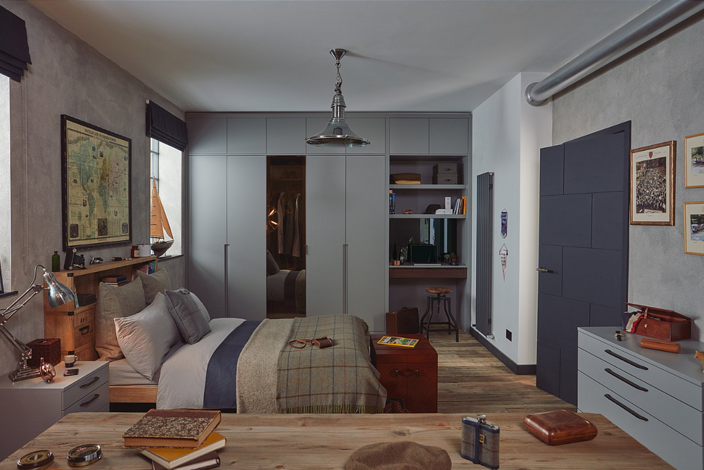 Bedroom with grey fitted wardrobes, open shelving, a timber desk and a dark blue door.