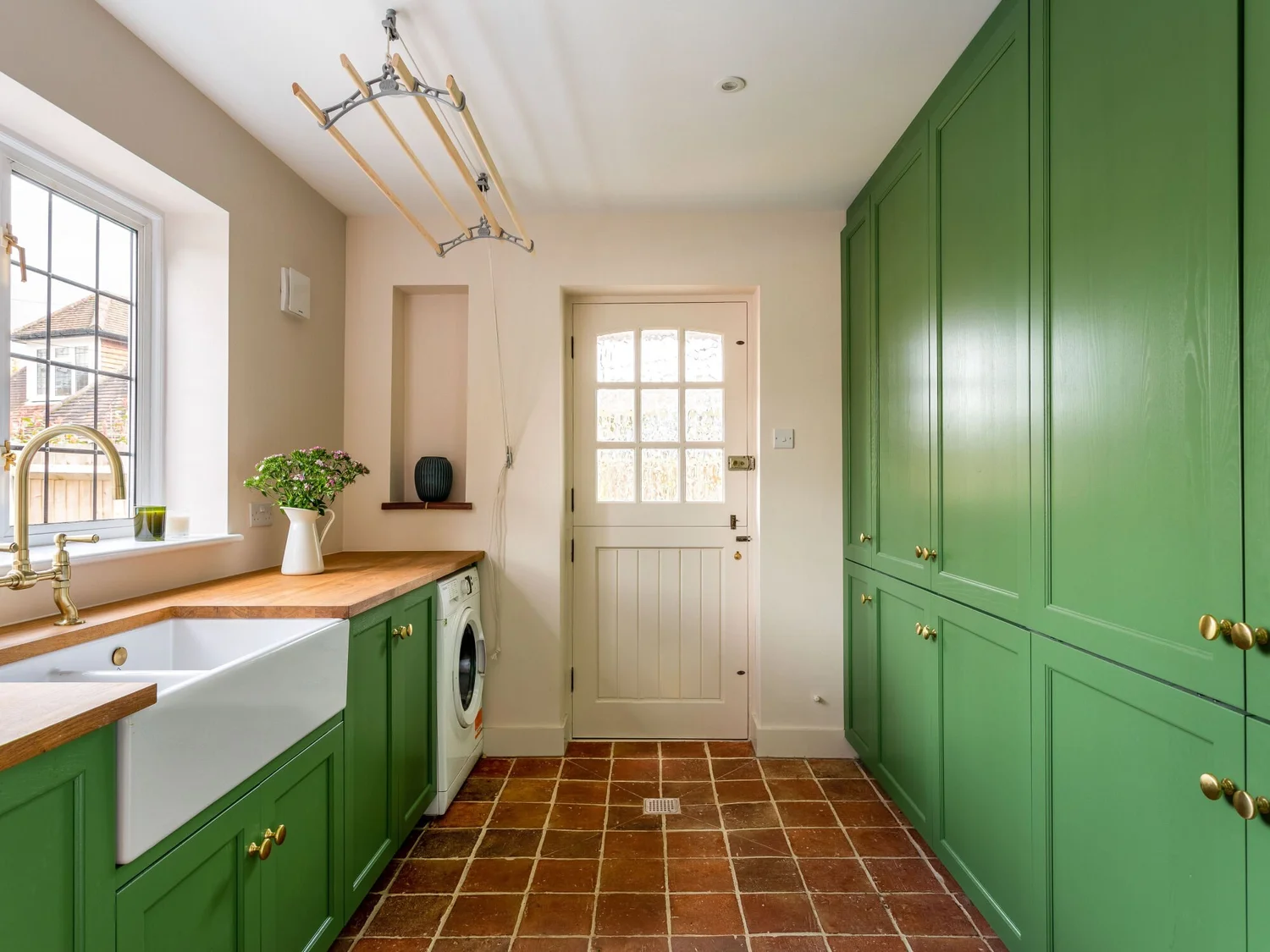 Green fitted utility room with tall storage and timber worktop
