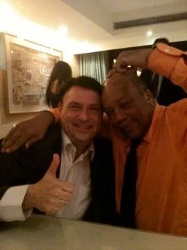 Two men smiling and posing for a photo in a restaurant or cafe, with a woman in the background.