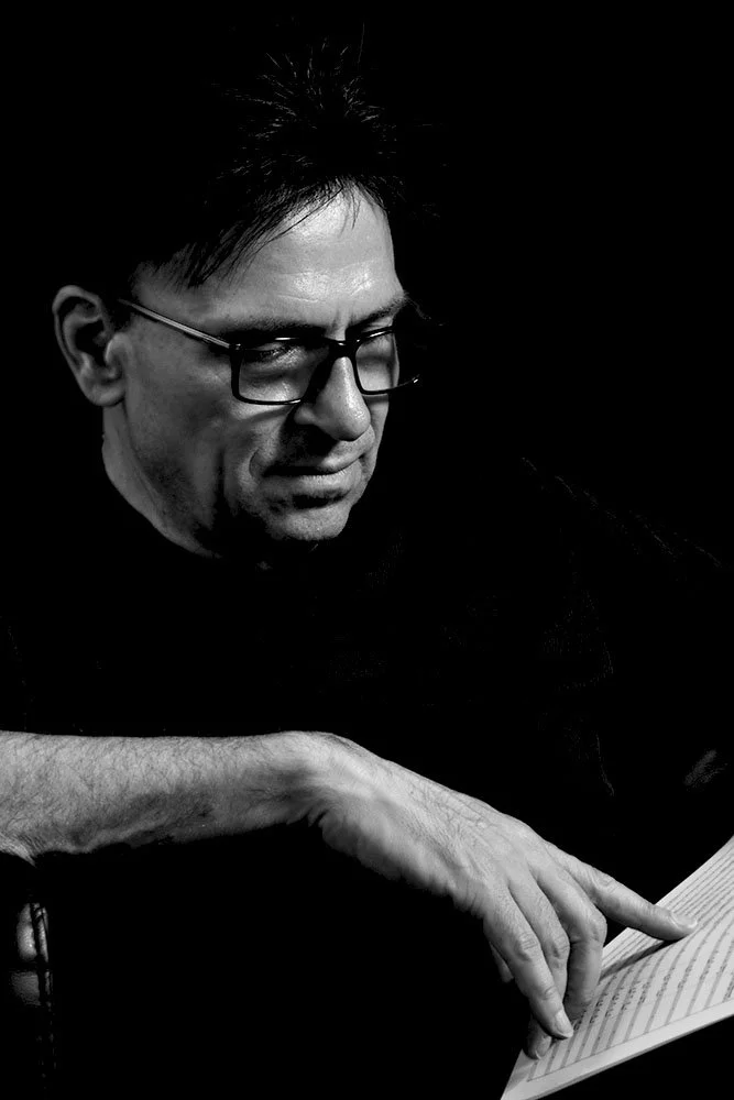 A black and white photo of a man with glasses, reading a book.