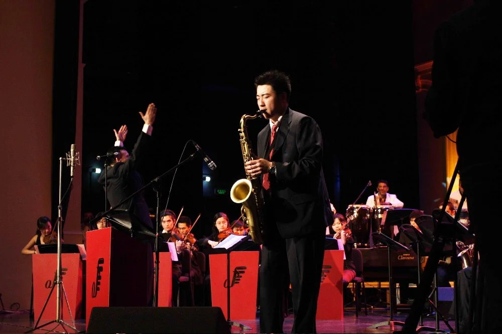 A jazz band performing on stage with a conductor and a saxophonist in the foreground.