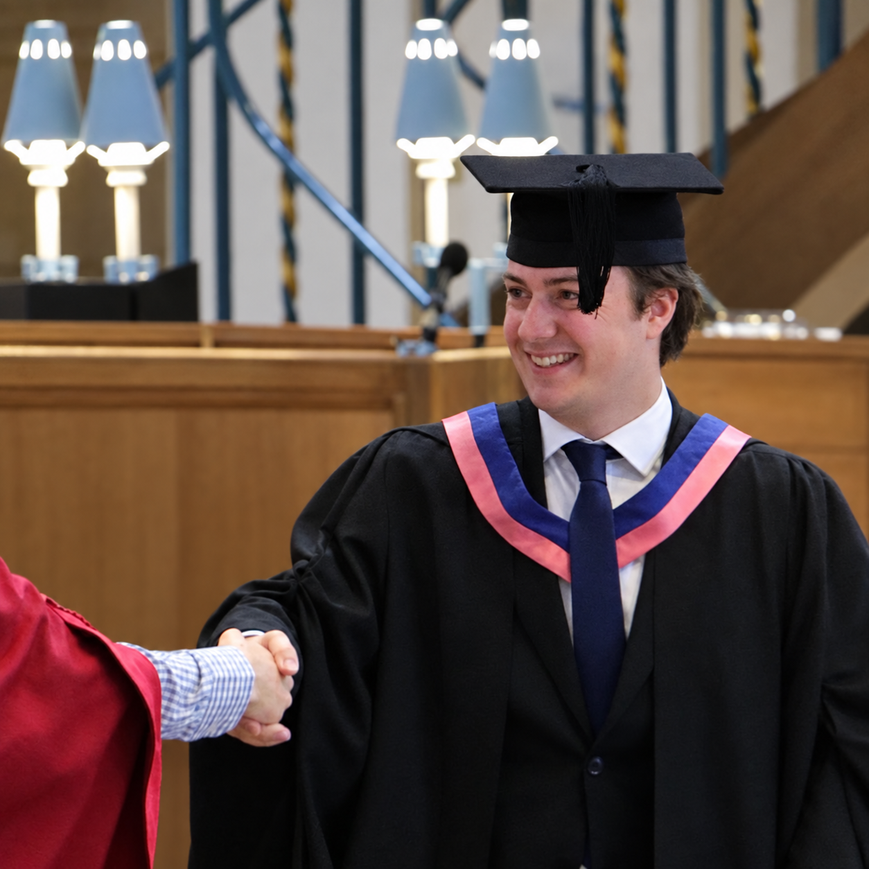 A young man in a graduation cap and gown shaking hands at a graduation ceremony.