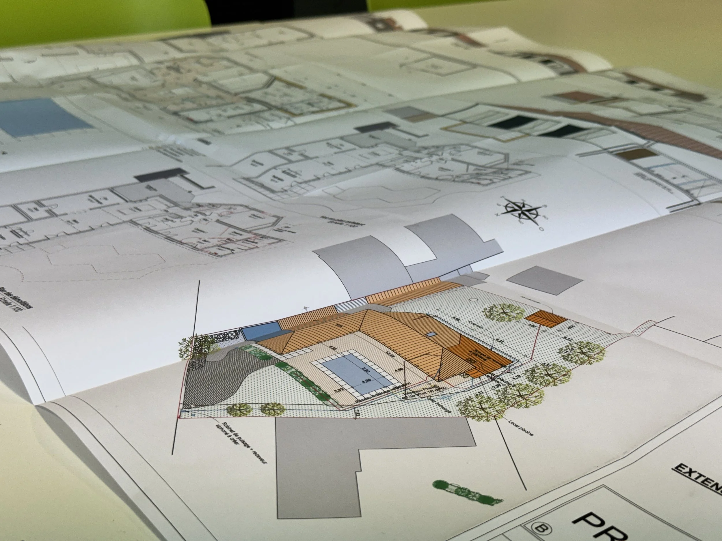 Plans d'architecture détaillés de bâtiments avec différentes sections, couleurs et annotations, posés sur une table.